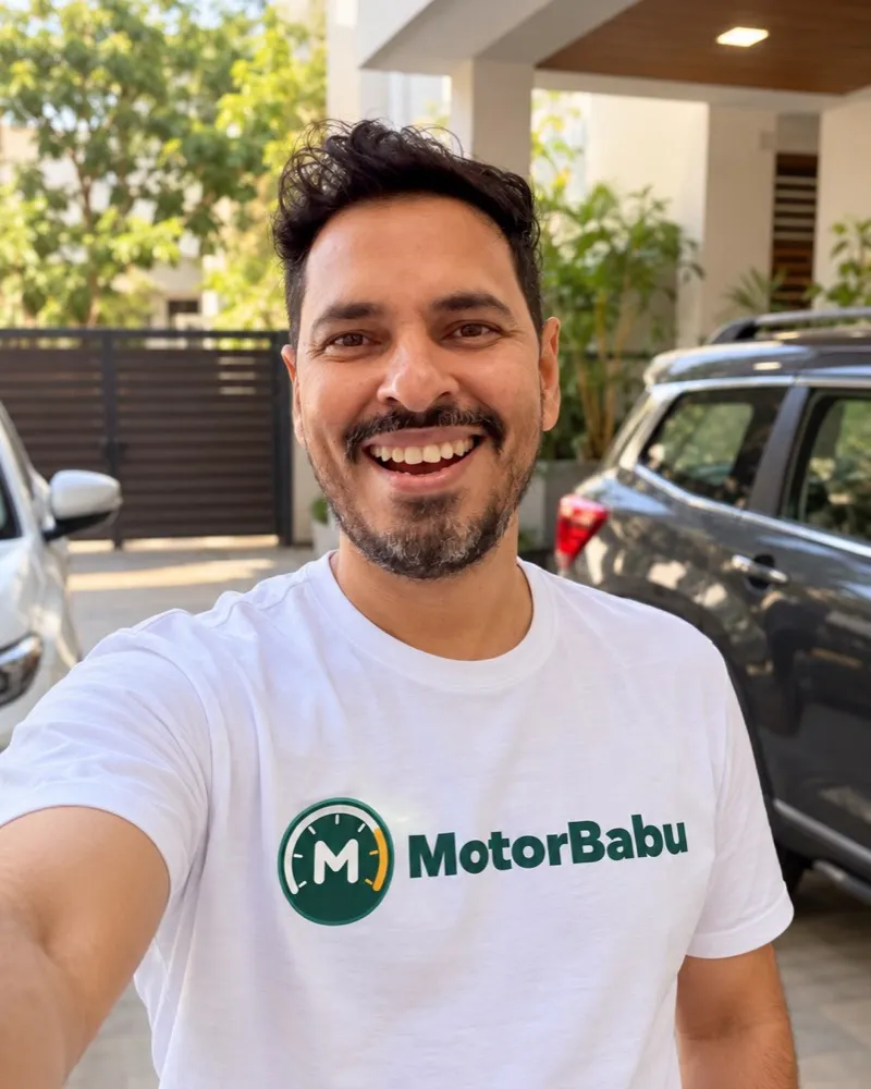 Avdhesh Solanki, founder of MotorBabu, smiling in a MotorBabu T-shirt in front of the family cars at home in Indore